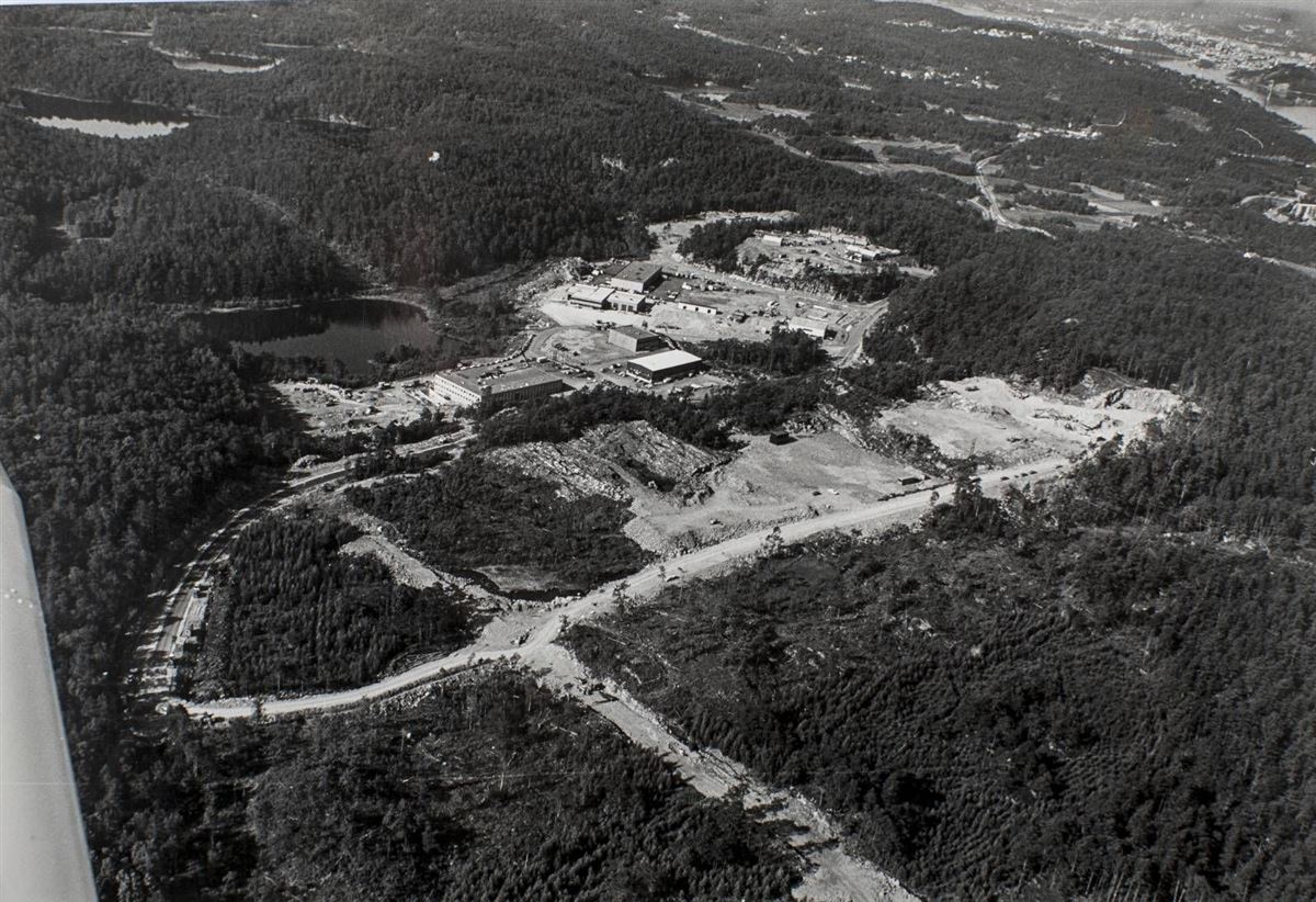 Flyfoto i svart-hvitt av de første byggene i Randesund industriområde, omgitt av skog og veier under bygging