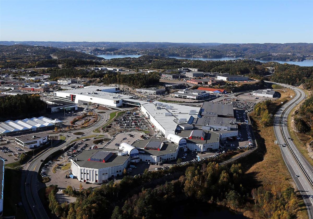 Flyfoto i farger av Sørlandssenteret og næringsbyggene rundt, med E18 til høyre og fjorden i bakgrunnen